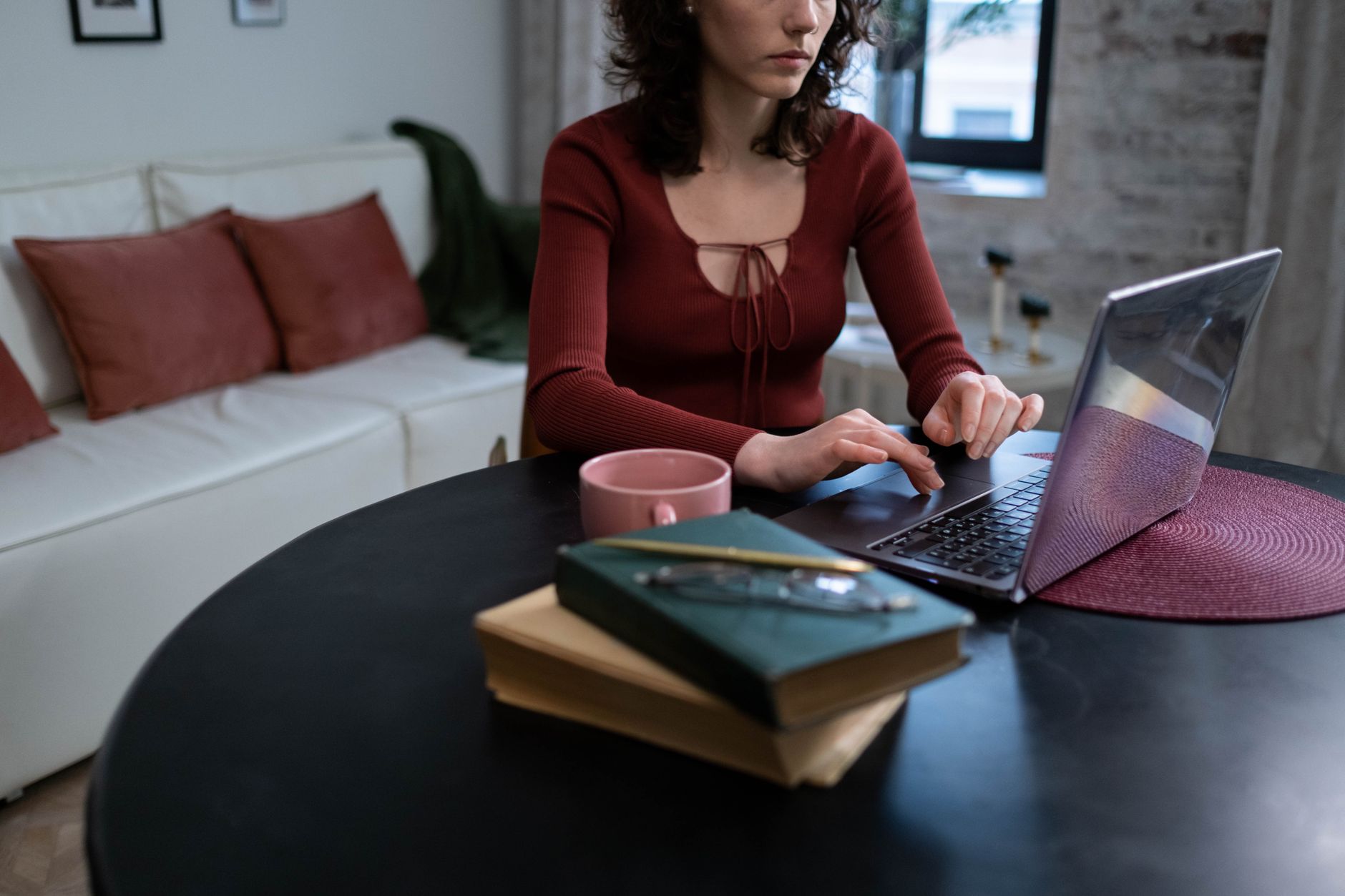 Une femme tape sur un ordinateur portable, assise à une table ronde noire dans une pièce élégante et confortable.