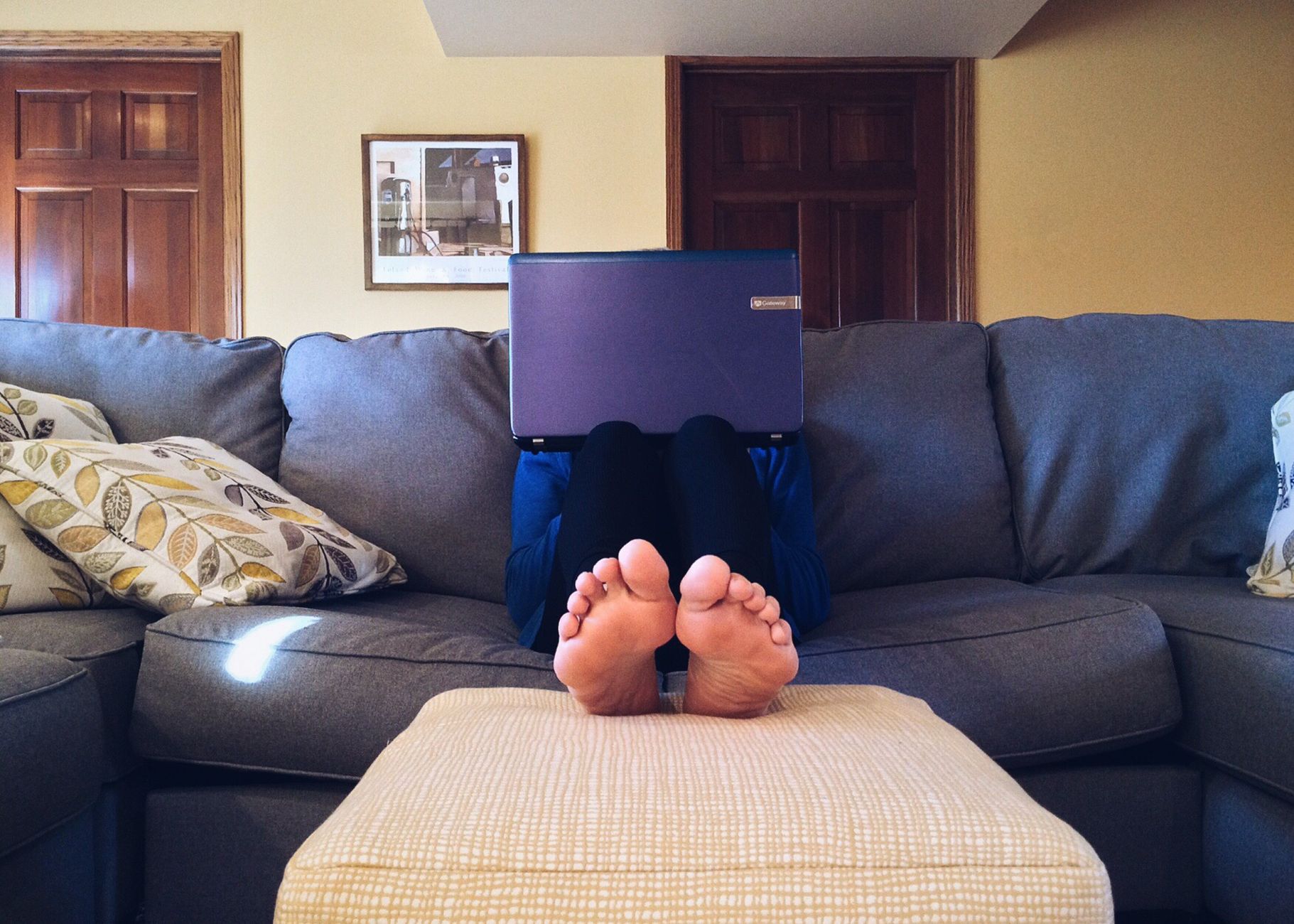 Personne se relaxant sur un canapé confortable avec un ordinateur portable, symbole du confort du travail à domicile moderne.