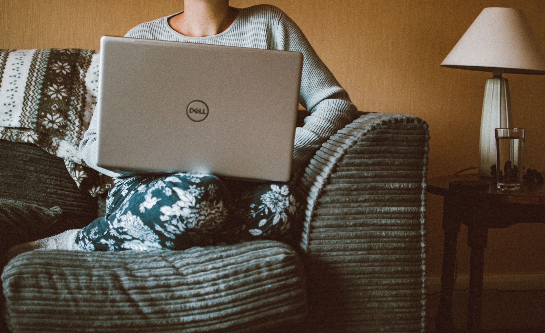Femme en sweat-shirt jaune utilisant un ordinateur portable à la maison, illustrant le travail à distance dans un intérieur cosy et moderne.